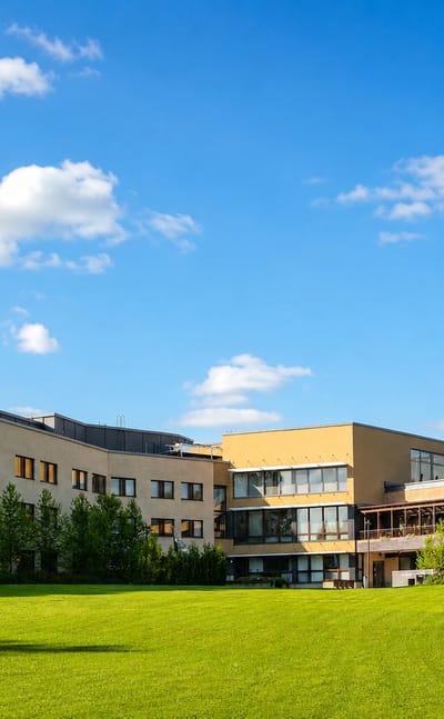 A modern beige low-rise building on a sunlit green lawn under blue summer skies in Taulumäki, Jyväskylä, Finland.