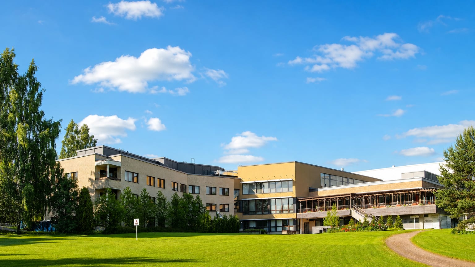 A modern beige low-rise building on a sunlit green lawn under blue summer skies in Taulumäki, Jyväskylä, Finland.