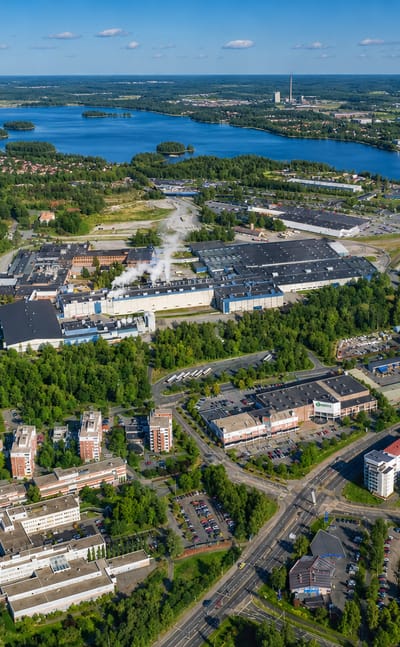 Aerial daytime view of Tourula in Jyväskylä, Finland: lakeside industrial complex with forests and residential apartment blocks.