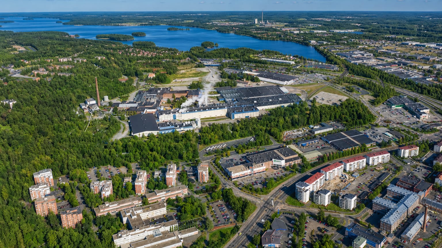 Aerial daytime view of Tourula in Jyväskylä, Finland: lakeside industrial complex with forests and residential apartment blocks.