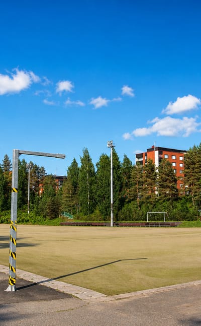 A floodlit sports field backed by pines and red-brick apartment blocks in Viitaniemi, Jyvaskyla.