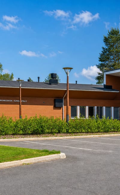 Modern wood-clad Kannonkoski municipal hall and its car park under a clear summer sky, central Finland.