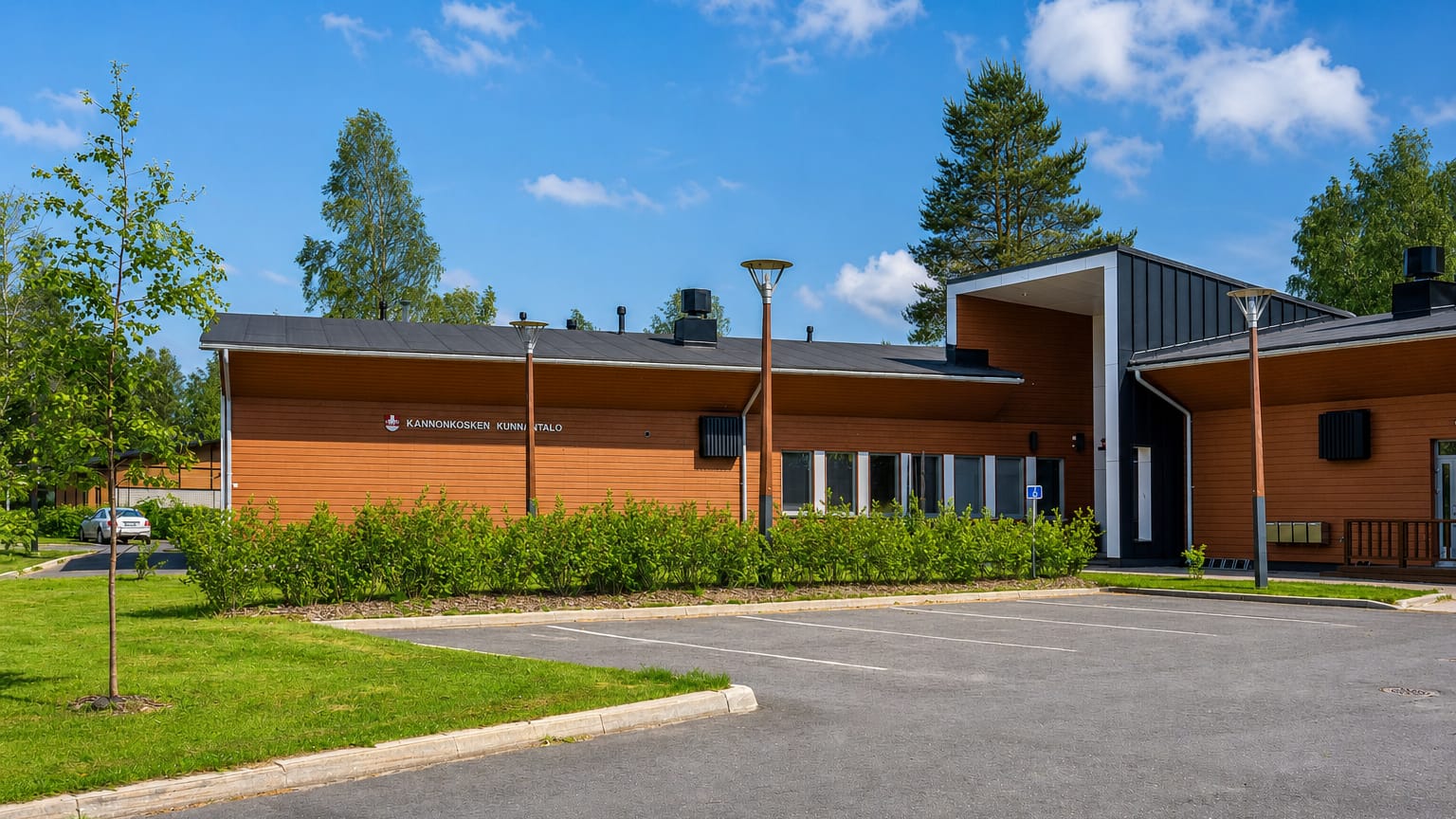 Modern wood-clad Kannonkoski municipal hall and its car park under a clear summer sky, central Finland.