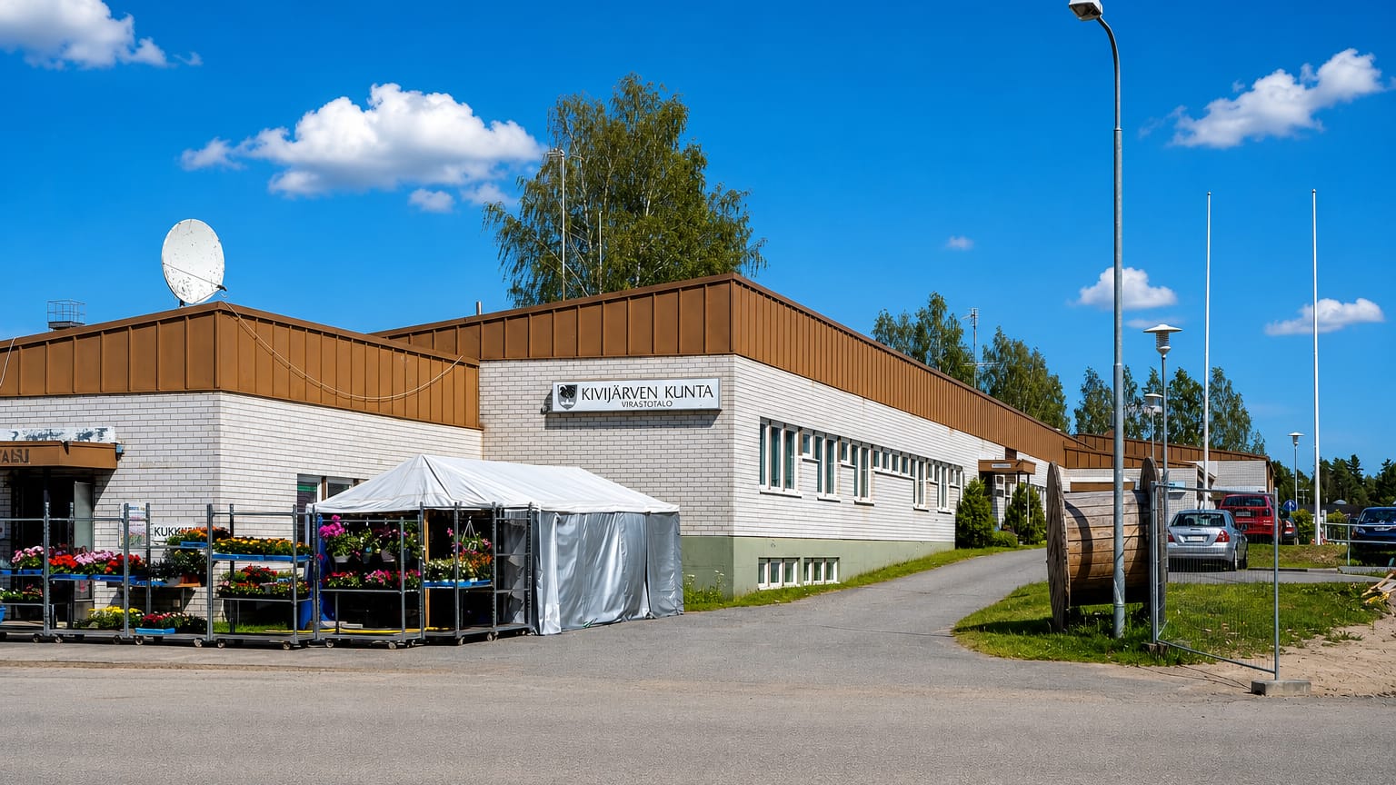 The Kivijärvi municipal office with a summer flower stall and parked cars, Finland.