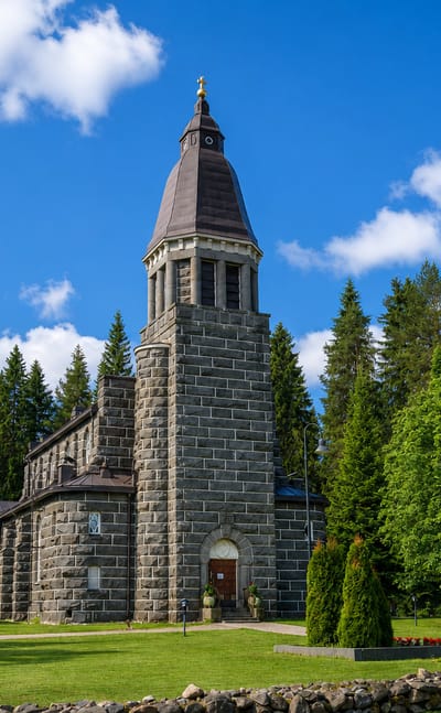 Konnevesi's grey granite church with a tall tower and copper spire ringed by pine forest in central Finland.