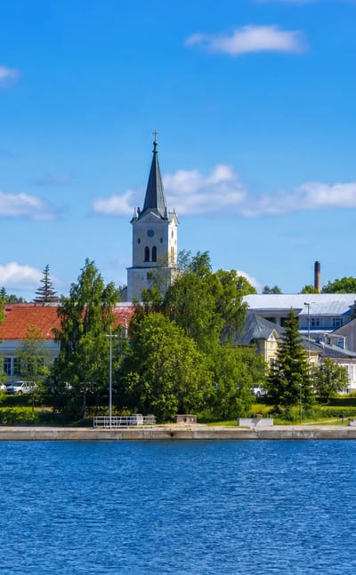 Lakeside skyline of Kyyjärvi with a white church spire, domed building and wooden houses among trees, Finland