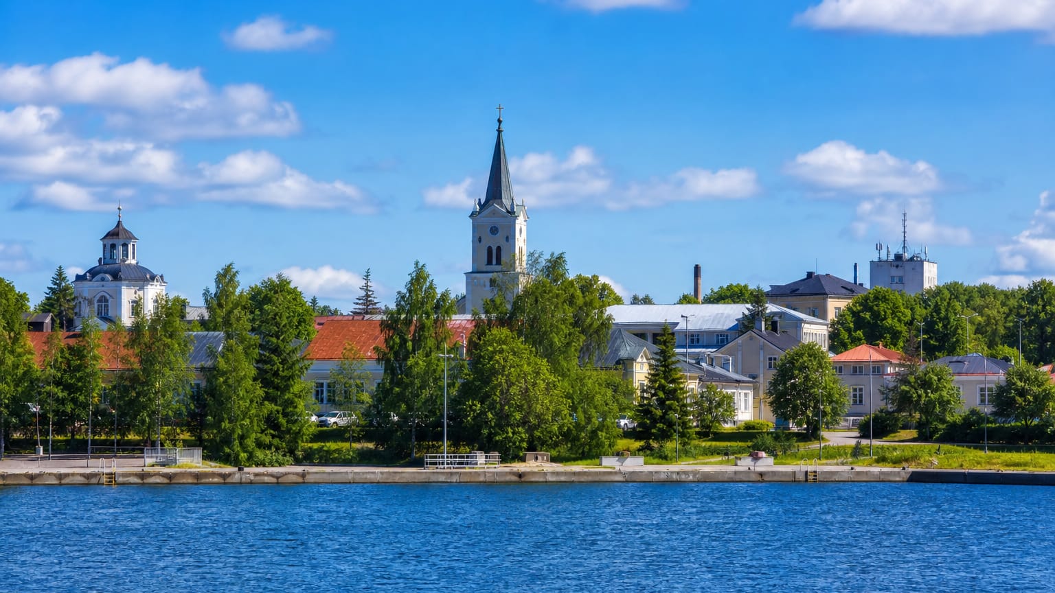 Lakeside skyline of Kyyjärvi with a white church spire, domed building and wooden houses among trees, Finland