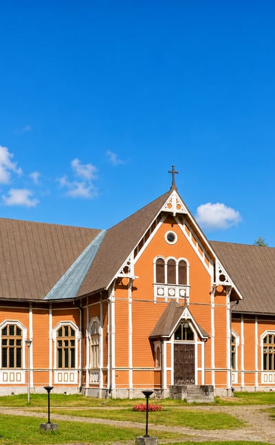 Ochre wooden Multia church with a tall spire and flower beds on a green lawn, central Finland.