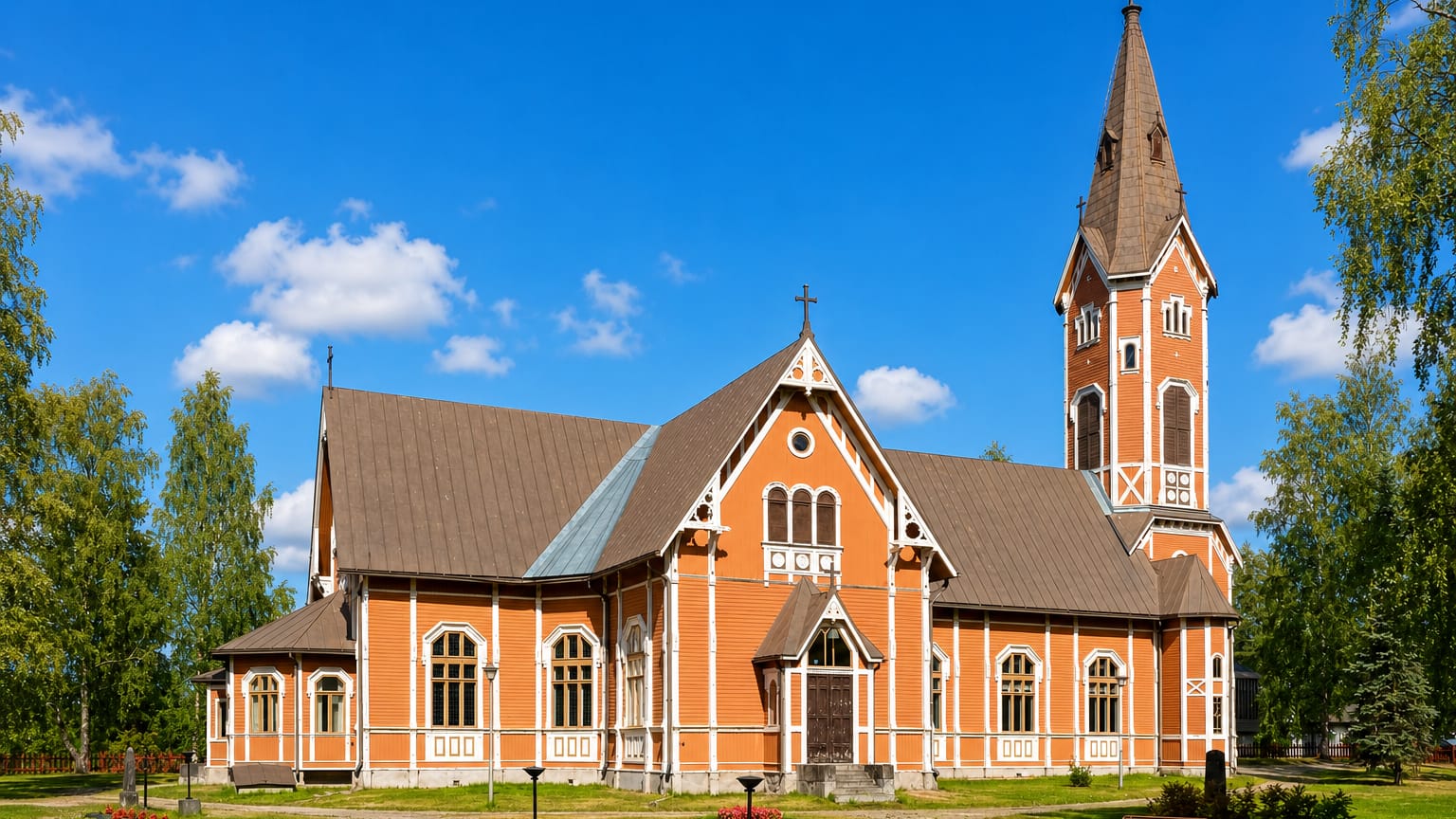 Ochre wooden Multia church with a tall spire and flower beds on a green lawn, central Finland.