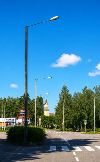 Quiet main-road crossing with a church spire rising over pine trees in the Finnish town of Pihtipudas.