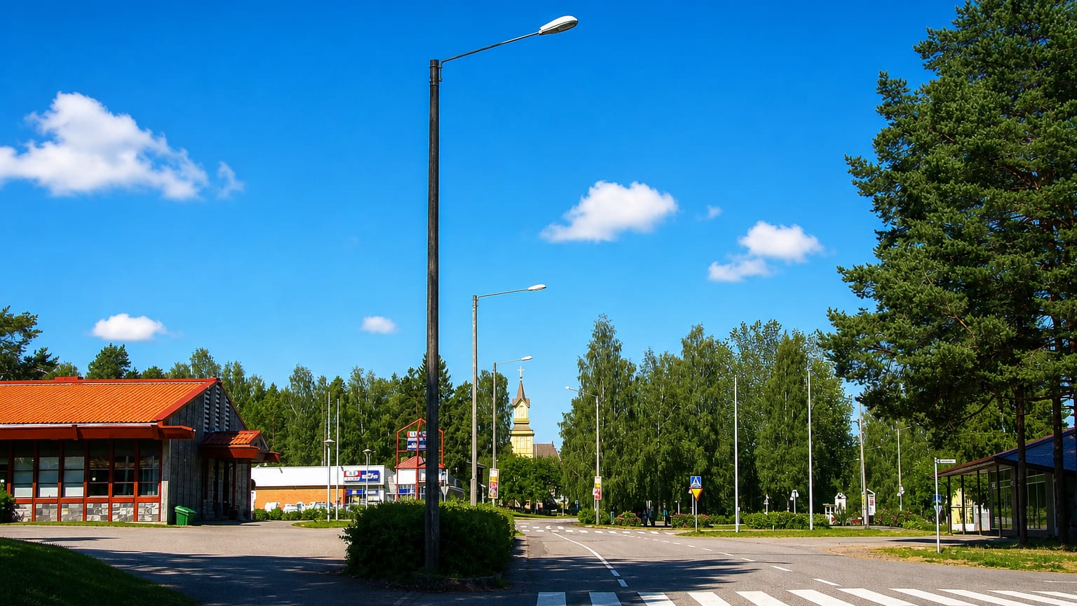 Quiet main-road crossing with a church spire rising over pine trees in the Finnish town of Pihtipudas.