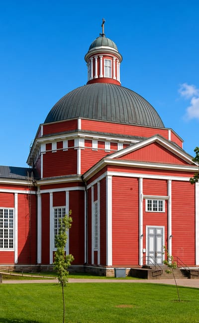 Red wooden neoclassical church with a dark dome set in green grounds in Saarijärvi, Finland.
