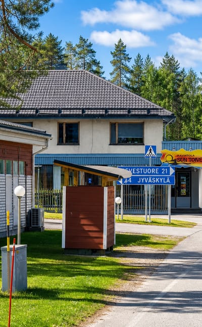 Roadside in Toivakka with a house, restaurant sign and a blue road sign to Jyvaskyla amid pine forest.