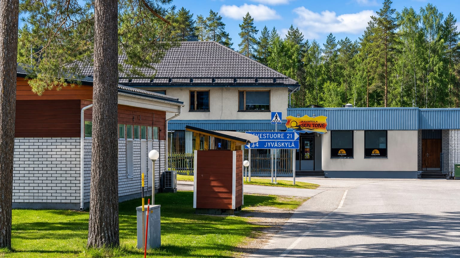Roadside in Toivakka with a house, restaurant sign and a blue road sign to Jyvaskyla amid pine forest.