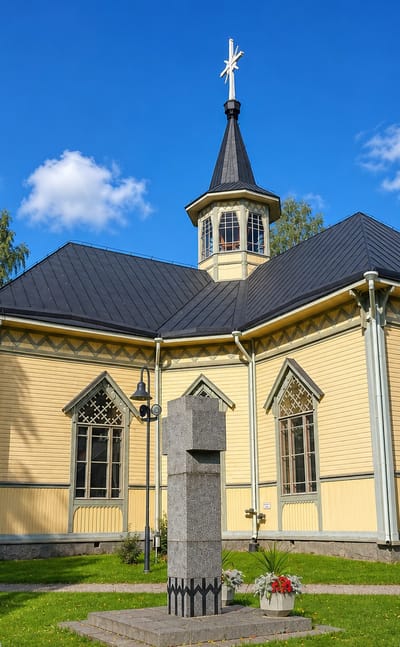 Uurainen's yellow wooden church with a dark steeple and cross under a blue summer sky in central Finland.