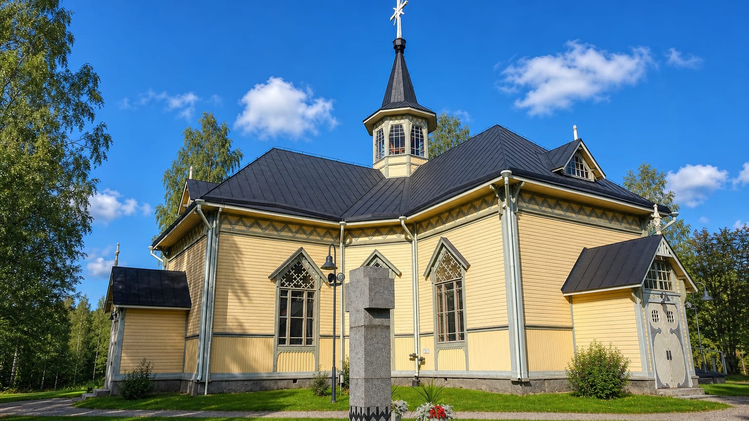 Uurainen's yellow wooden church with a dark steeple and cross under a blue summer sky in central Finland.