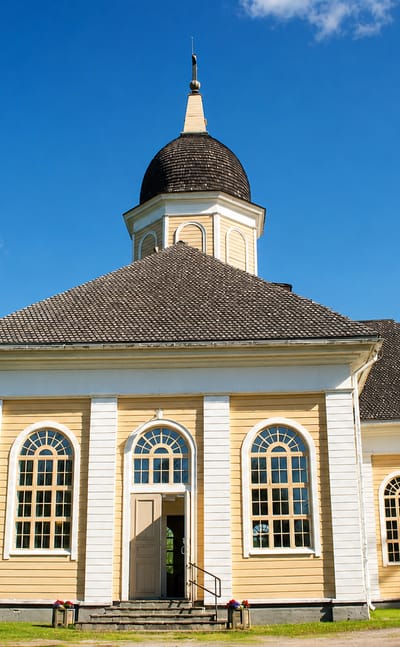 Yellow and white wooden church with a domed bell tower under a blue sky in Hyrynsalmi, Finland.