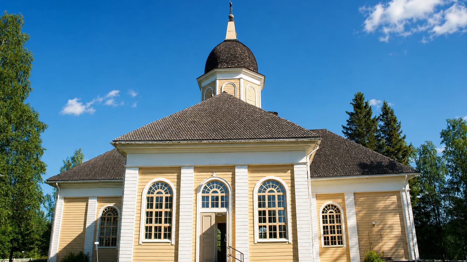 Yellow and white wooden church with a domed bell tower under a blue sky in Hyrynsalmi, Finland.