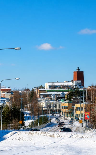Snowy winter street leading into Kajaani with its red-brick tower building under a clear blue sky