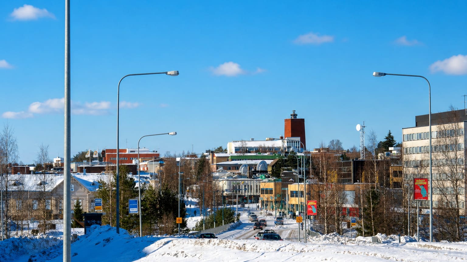 Snowy winter street leading into Kajaani with its red-brick tower building under a clear blue sky