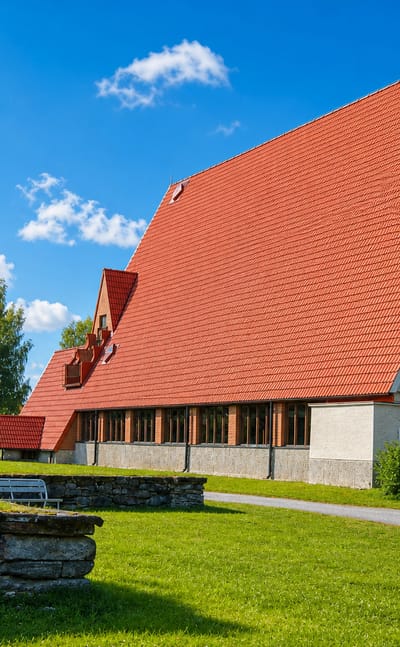 Modern church with a steep red-tiled roof and pale gable in Puolanka, Finland, set on a green lawn.