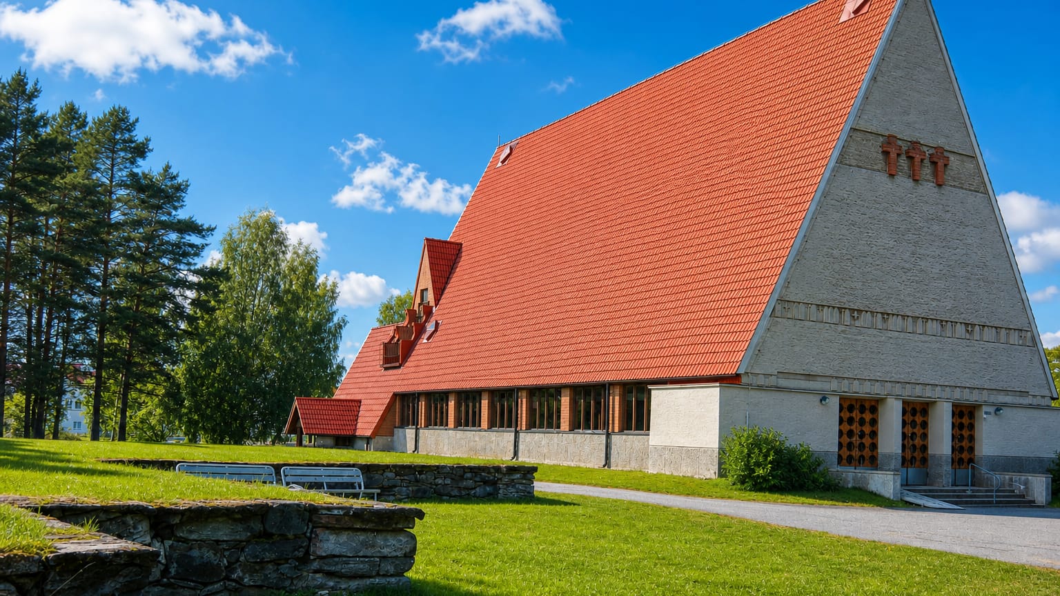 Modern church with a steep red-tiled roof and pale gable in Puolanka, Finland, set on a green lawn.