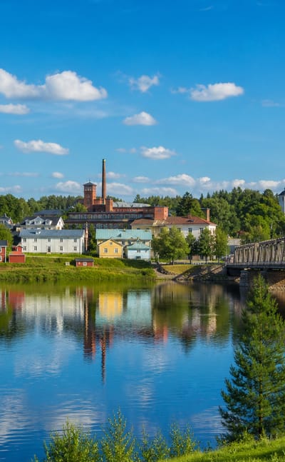 Summer townscape of Vaala, Finland, with a yellow church, brick tower and iron truss bridge mirrored in calm river water