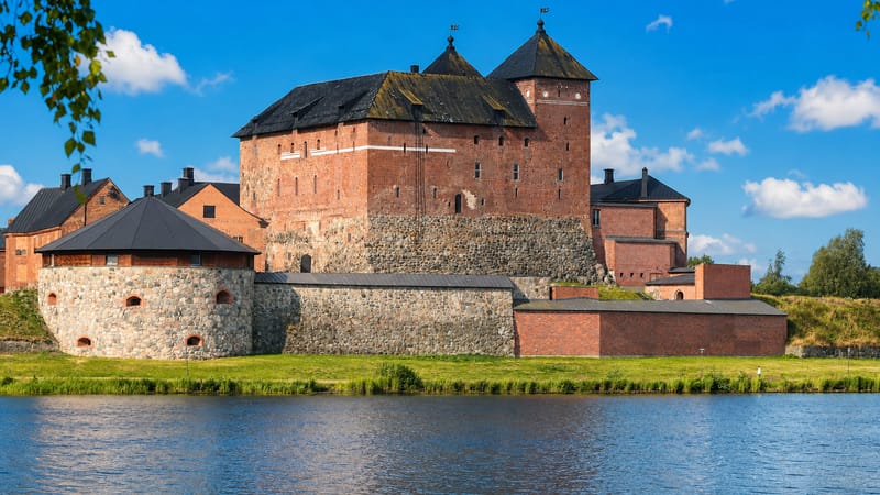 Häme Castle's red-brick keep and grey stone bastions rising above the lakeshore in Hämeenlinna, Finland