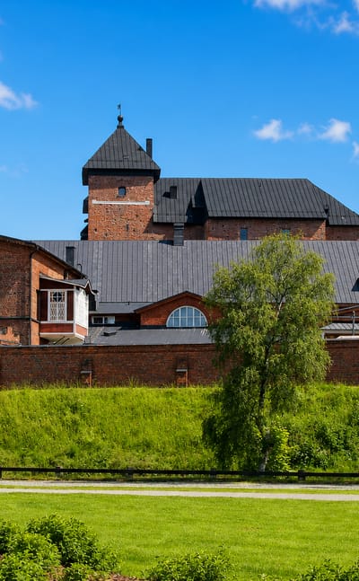 Linnanniemi in Hämeenlinna, where the red-brick castle and its walled outbuildings stand above a green park.