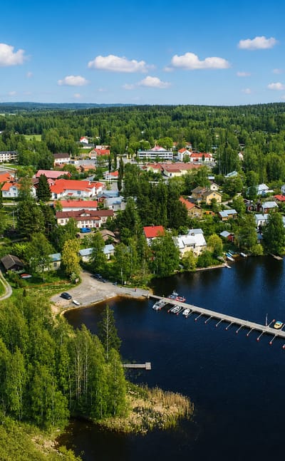 Aerial view of Hauho, Finland: a lakeside village with a church spire, marina and red-roofed houses by forested shores.