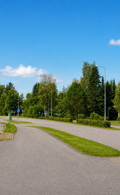 Roadside view in Humppila with a yellow shop building, flagpole and green summer trees under a blue sky.