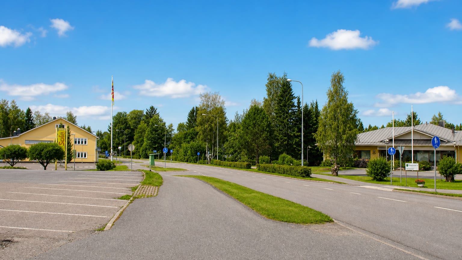 Roadside view in Humppila with a yellow shop building, flagpole and green summer trees under a blue sky.