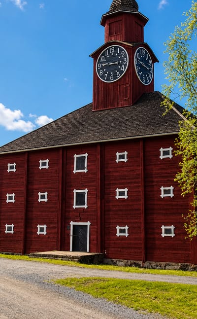Jokioinen's distinctive red wooden granary with a twin-faced clock tower beside a gravel road in summer.
