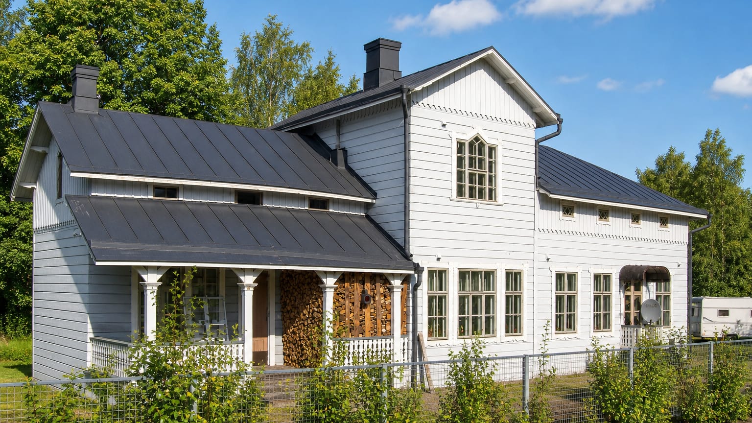 White wooden house with a black metal roof and covered porch on the edge of Oitti, Finland.