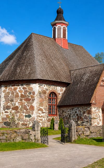 Medieval fieldstone church with a red belfry tower and shingled roof in Renko, Finland.