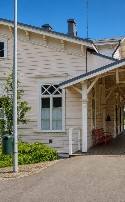Historic cream wooden railway station with a covered platform and red bench in Turenki, Finland.