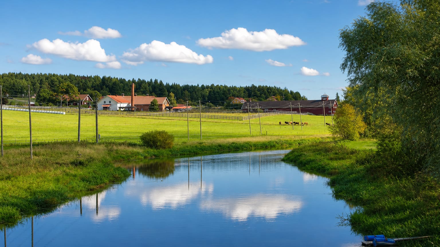 Calm river winding past green pastures and farm buildings in rural Ypäjä, Kanta-Häme, Finland.