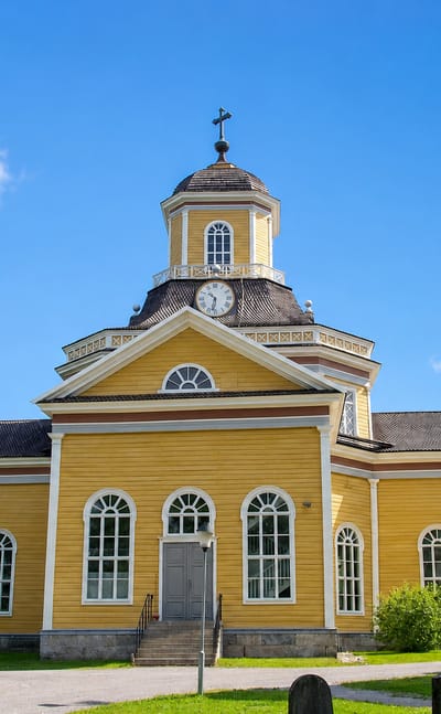 Yellow wooden church with a clock-topped lantern dome under blue sky in Kaustinen, Finland