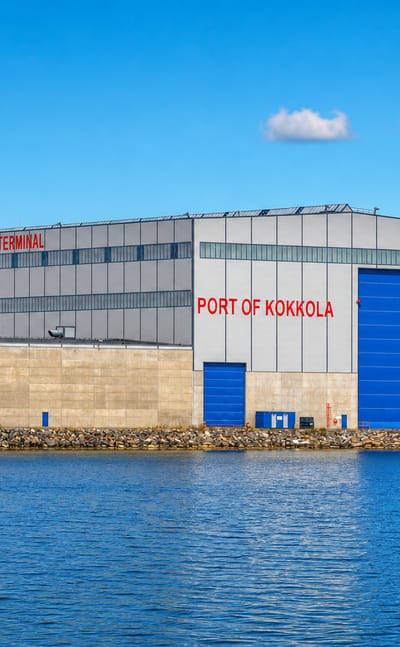 Port of Kokkola All Weather Terminal beside the harbour water under a clear blue sky, autumn trees on the far shore