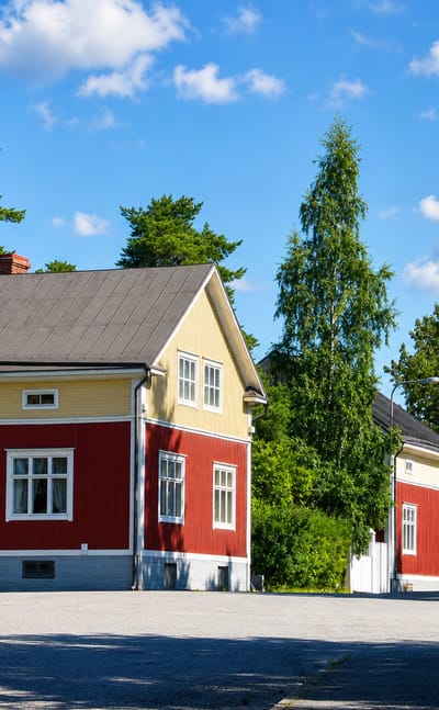 Red and yellow wooden houses among pines on a quiet street in Mantykangas, Kokkola.