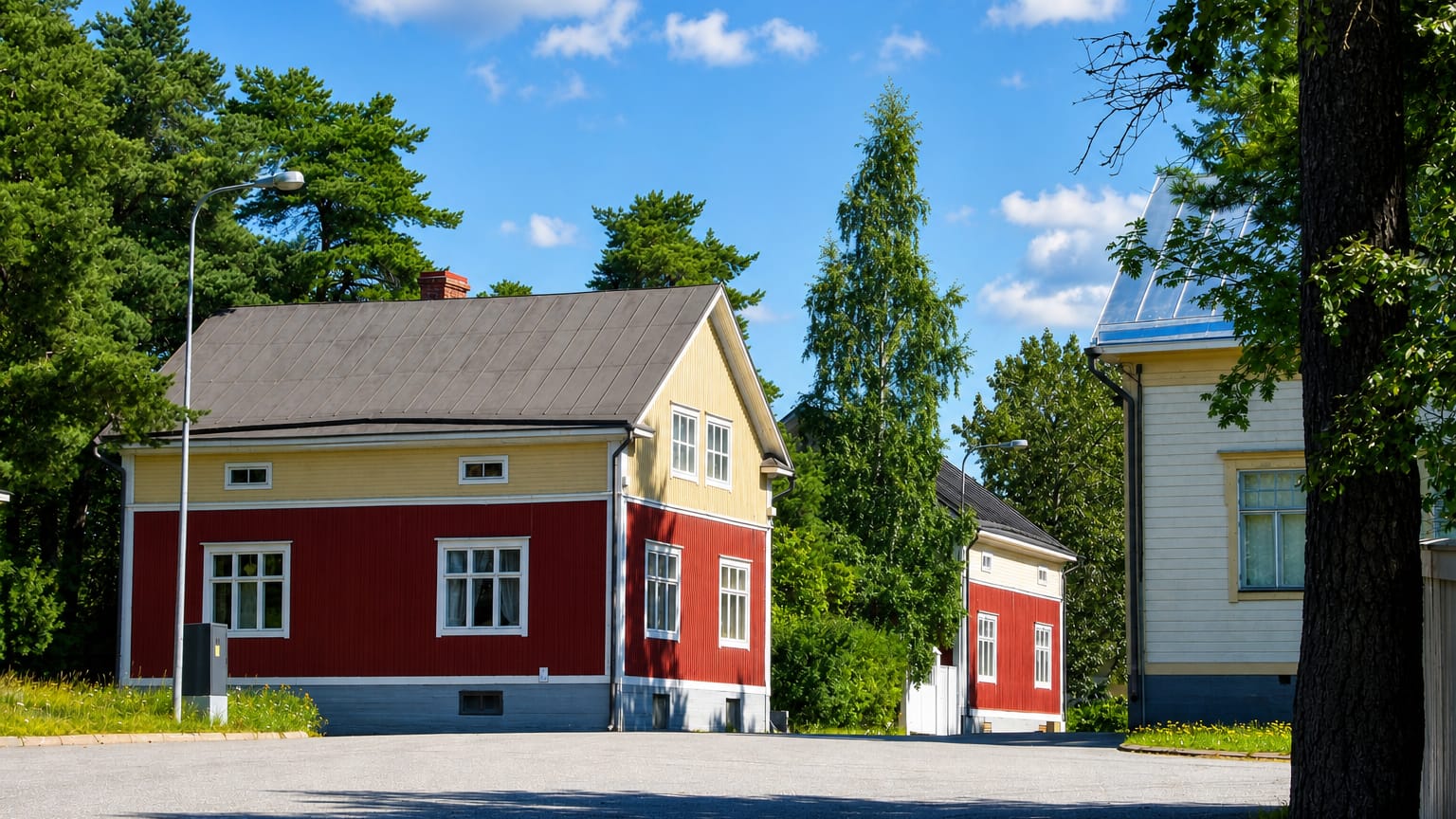 Red and yellow wooden houses among pines on a quiet street in Mantykangas, Kokkola.