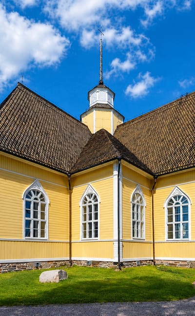 Yellow wooden church with a shingled roof, central lantern spire and Gothic-arched windows in Lohtaja, Finland.
