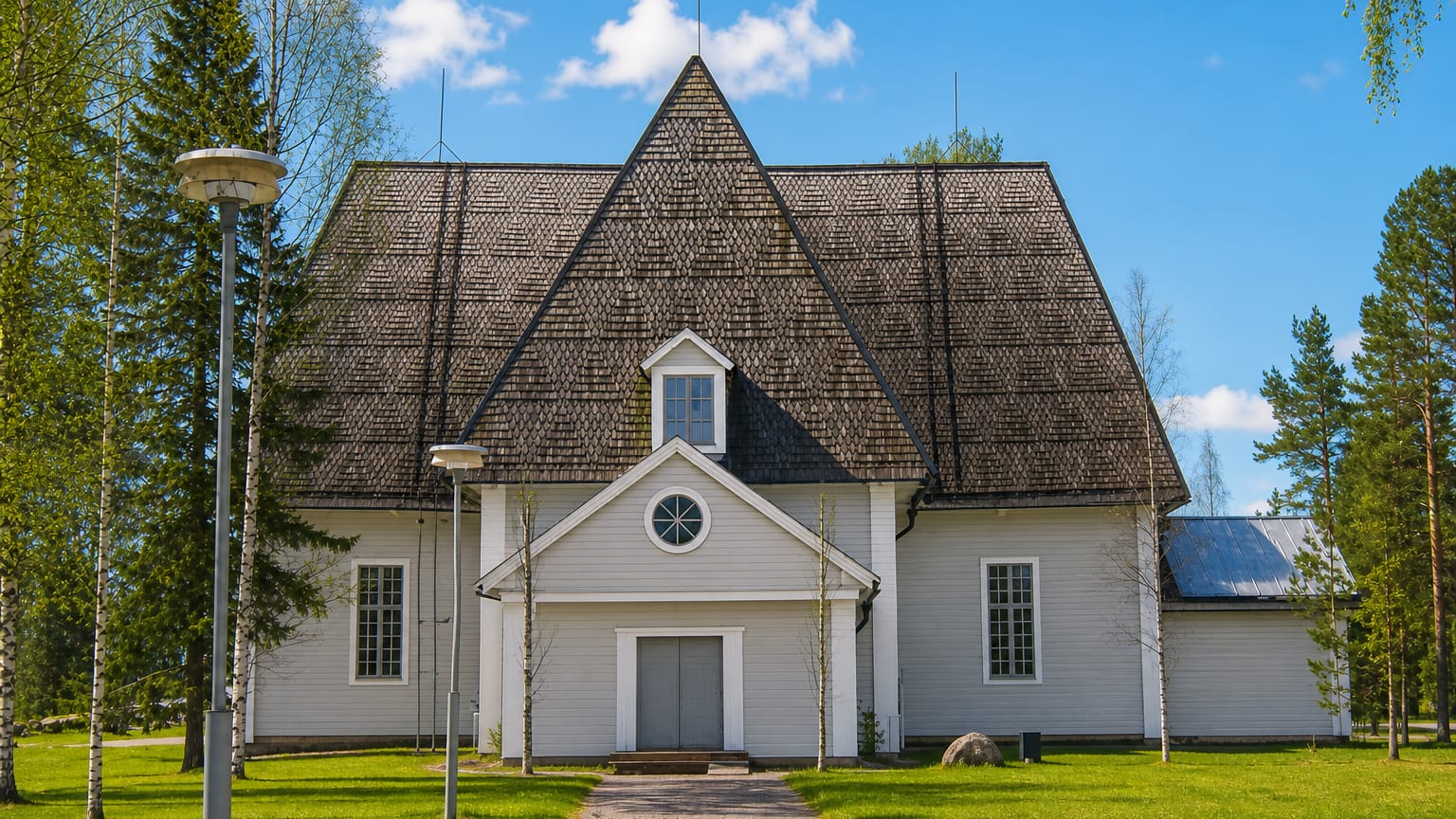 Elimaki's large white wooden church with a steep shingled roof and birch-lined path under a blue sky.