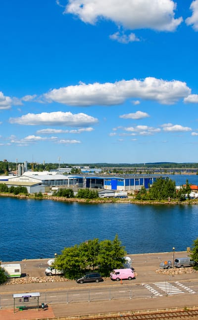 Kotka harbour waterfront with a rail yard, moored boats and industrial buildings on an island under a bright blue summer sky