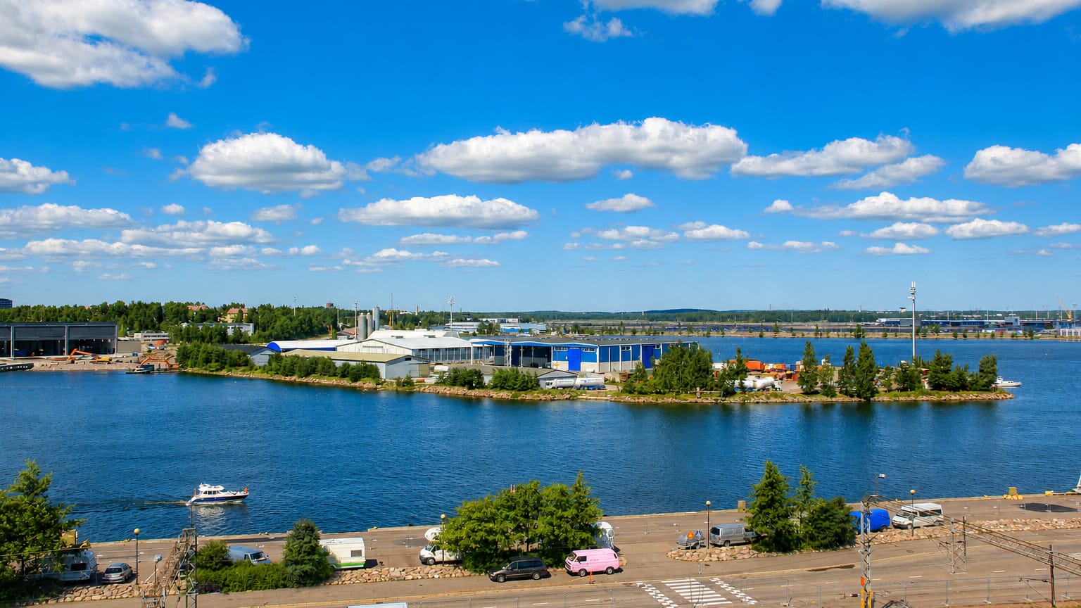 Kotka harbour waterfront with a rail yard, moored boats and industrial buildings on an island under a bright blue summer sky