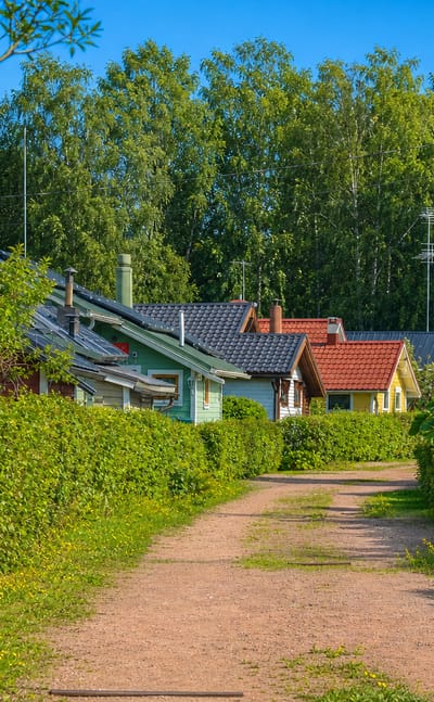 Hedge-lined gravel lane past timber houses in the Korela neighbourhood of Kotka in summer.