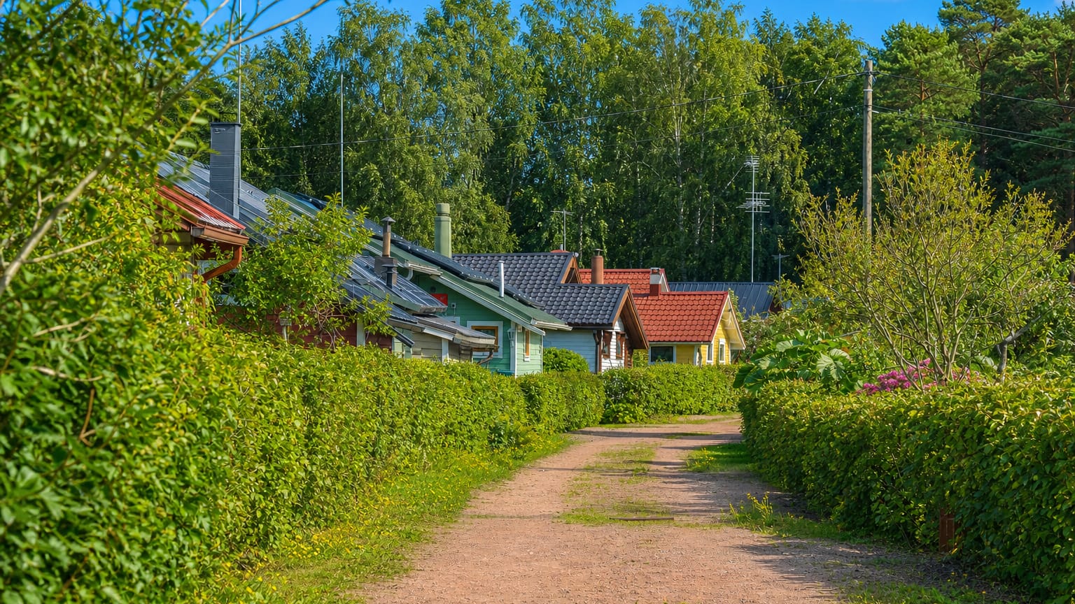 Hedge-lined gravel lane past timber houses in the Korela neighbourhood of Kotka in summer.