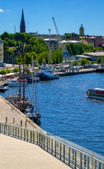 Harbour quay at Kotkansaari, Kotka, with cranes, a moored tall ship, a church spire and a hilltop tower.
