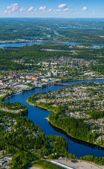 Aerial view of Kouvola, Finland, a low-rise town amid dense forest with a river winding through and lakes beyond.