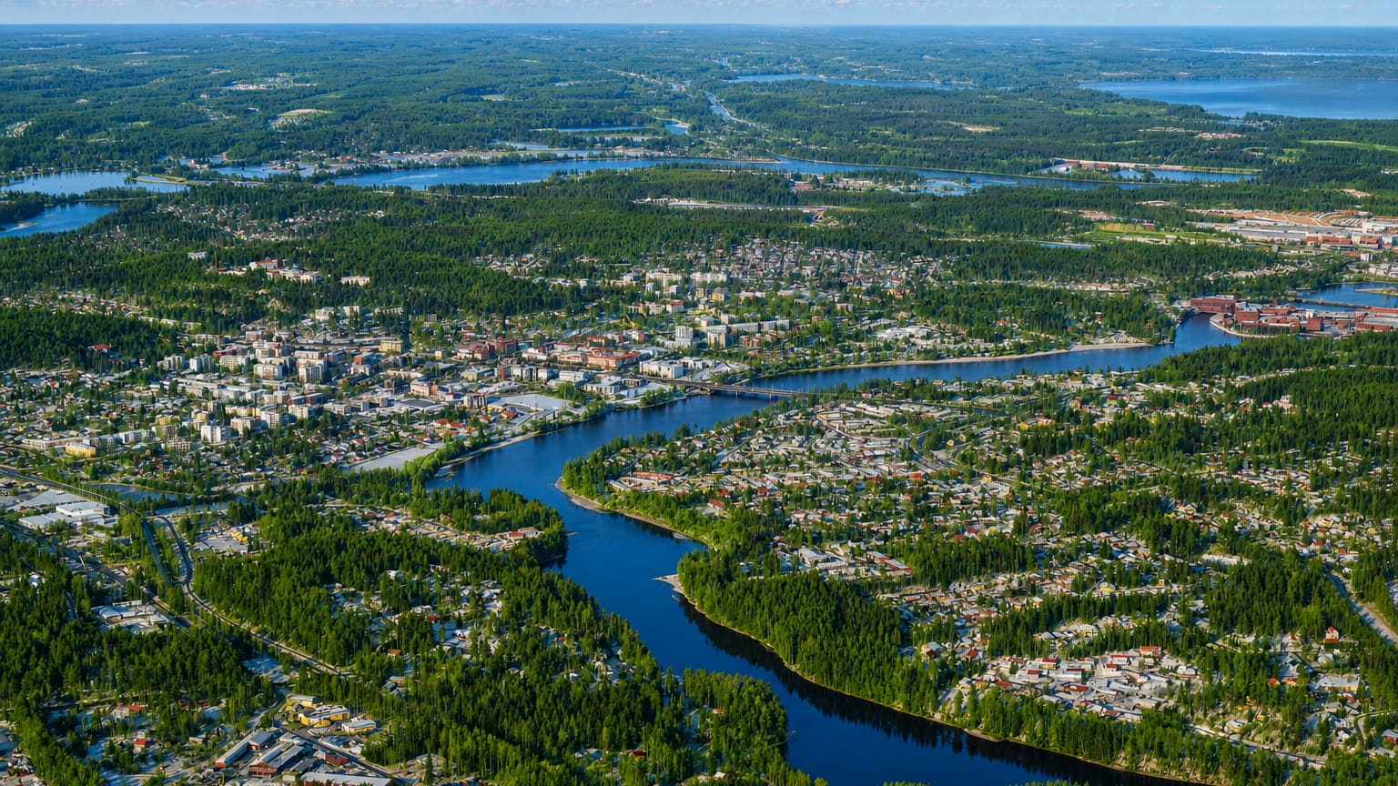 Aerial view of Kouvola, Finland, a low-rise town amid dense forest with a river winding through and lakes beyond.